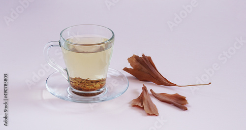 glass cup of tea on light pink background with dried yellow gingko biloba leaves. copy space. top view