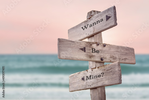 wanna be mine text quote written on wooden signpost by the sea. Positive pink turqoise pastel theme.