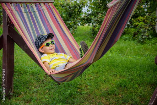 Cute little Caucasian boy relaxing and having fun in multicolored hammock in backyard or outdoor playground. Summer active leisure for kids. Child swinging on hammock. Activities for children