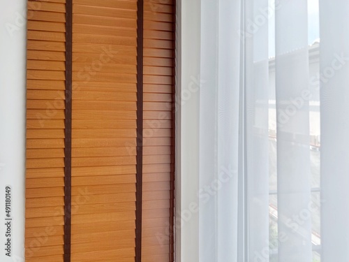 White sheer curtains with translucent fabric and wooden blinds hanging on window.