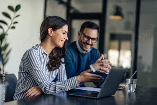 Laughing caucasian colleagues, checking the company budget on their laptops.