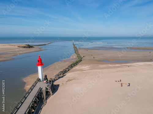 Bord de mer avec des personnes dans le sable photographié en drone à côté d'un ponton et d'un phare. 