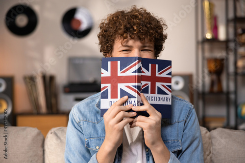 A teenager with curly hair sits focused in a room studying for an English exam. A boy in a blue jean shirt prepares for an English job interview.