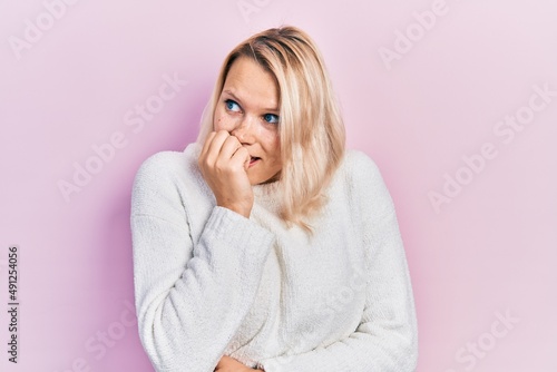 Beautiful caucasian blonde woman wearing casual winter sweater looking stressed and nervous with hands on mouth biting nails. anxiety problem.