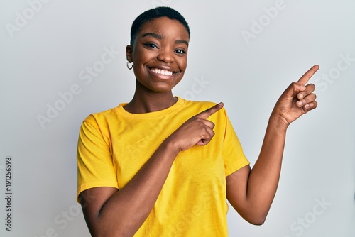 Young african american woman wearing casual yellow t shirt smiling and looking at the camera pointing with two hands and fingers to the side.