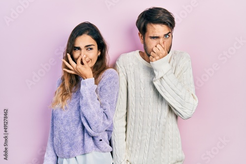 Young hispanic couple wearing casual clothes smelling something stinky and disgusting, intolerable smell, holding breath with fingers on nose. bad smell