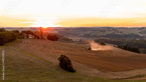 Moissonneuse batteuse ramassant le blé au coucher du soleil dans la campagne gersoise en été