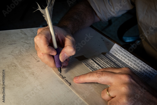Closeup view of the hands of a Jewish scribe holding a feather quill and writing the words of the Shema Yisrael prayer on parchment for a mezuzah that will be placed on the door of a Jewish home.