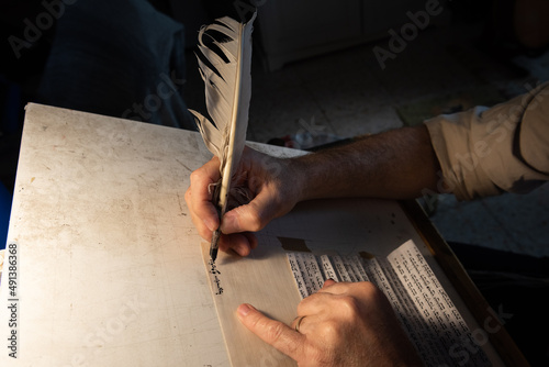 Closeup view of the hands of a Jewish scribe holding a feather quill and writing the words of the Shema Yisrael prayer on parchment for a mezuzah that will be placed on the door of a Jewish home.