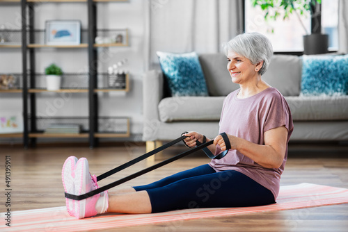 sport, fitness and healthy lifestyle concept - smiling senior woman exercising with resistance band on mat at home