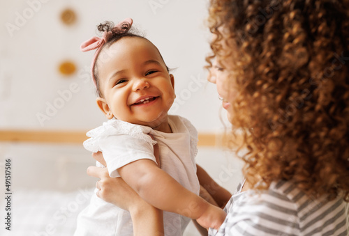 Happy, cheerful ethnic mom holds a laughing baby daughter in her arms.