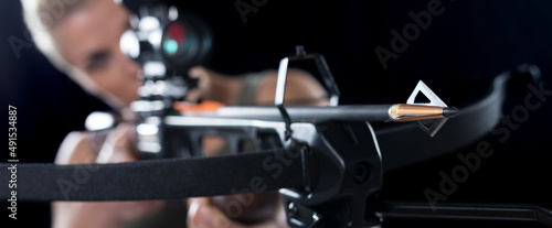 Young woman shooting with crossbow isolated on black background.