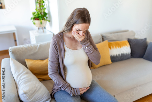 Pregnant woman suffering during her pregnancy, with back pain and headaches. Pregnant woman sitting on the sofa holding her belly with worried face expression.