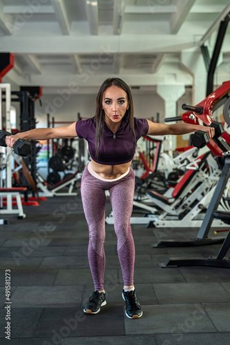 Young slim woman doing exercise lifting dumbbells in gym