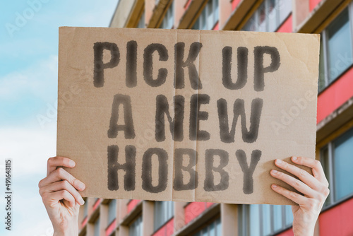 The phrase " Pick up a new hobby " on a banner in men's hands with blurred background. Perspective. Playing. Skill. Smart. Experience. Talent. Mind. Ability. Success. Successful. Start. Study