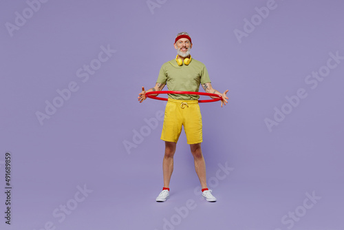 Full size body length sporty elderly gray-haired bearded man 40s years old in headband khaki t-shirt hold exercise with sports hoop isolated on plain pastel light purple background studio portrait
