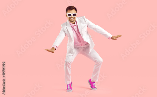 Happy millennial guy in suit and pink converse dance on pink studio background. Smiling stylish young Caucasian man in formalwear and tennis shoes make moves have fun. Fashion and style.
