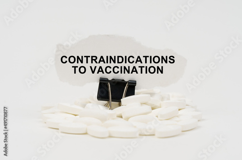 On a white surface are pills and torn paper with the inscription - contraindications to vaccination