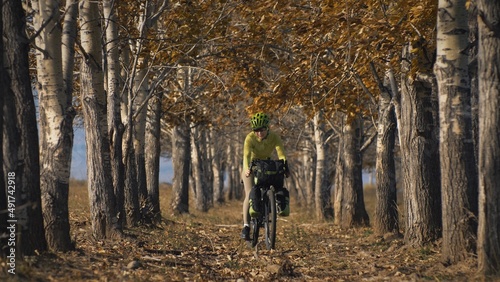 The woman travel on mixed terrain cycle touring with bikepacking. The traveler journey with bicycle bags. Sportswear in green black colors. The trip in magical autumn forest, arch, alley, avenue.
