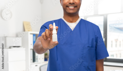 healthcare, profession and medicine concept - close up of happy smiling doctor or male nurse in blue uniform with nasal spray over medical office at hospital background