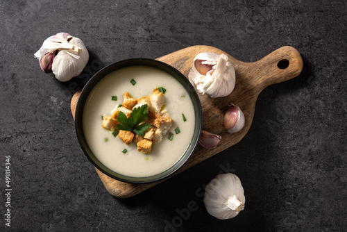 Garlic soup topped with croutons in bowl on black background