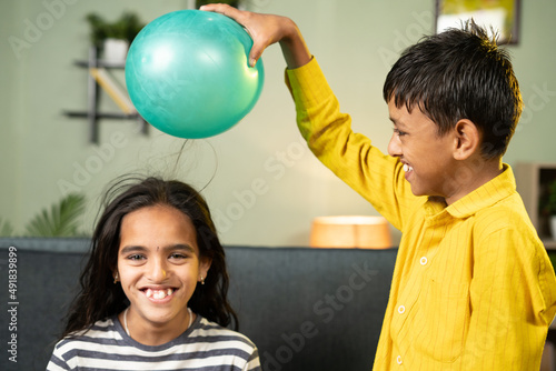 Focus on boy, Kids enjoys static cling experiment by playing while rubbing ballon to hair and hairs attracted to ballon - conept of excitement and home science experiment.