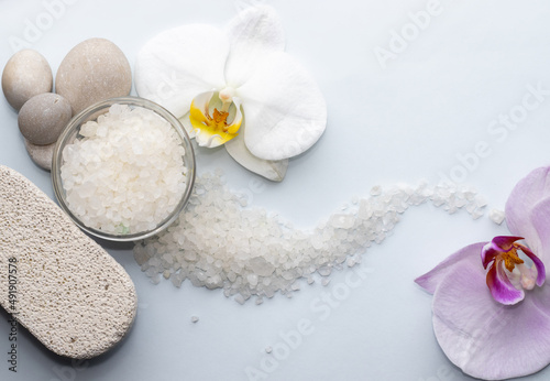 purple orchid flower on light blue background and sea salt. spa and skincare concept. relax, meditation mood. natural. mineral grains, wellnes.space for text. sea salt arranged wave shape.