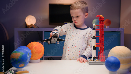 Little blonde boy kid plays with space shuttle from constructor, flies near planets of solar system in evening. Child imagines himself as pilot of spaceship. Desire fly in space, flying on spaceship.
