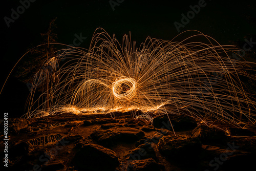 Goldene Funken sprühen nachts bei Steine Felsen Pfütze reflektiert die Funken durch glühende Stahlwolle die im Kreis geschleudert wird, Deutschland