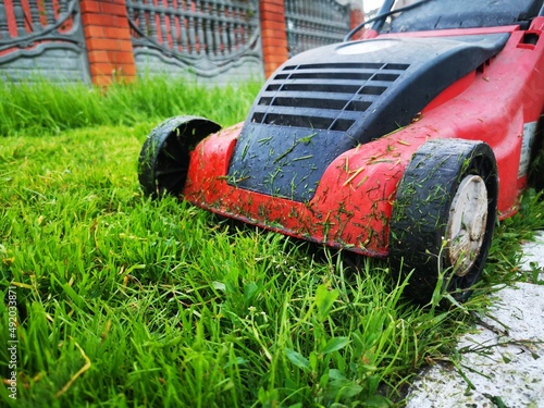 Lawn mower on green grass. A man cuts a thick lawn. Garden care, landscape improvement. Garden equipment. Electric grass trimmer. Removal of plants and weeds. horizontal photo