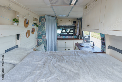 bright white and brown interior of a self made camper van transporter with bed, cupboard and kitchen sink