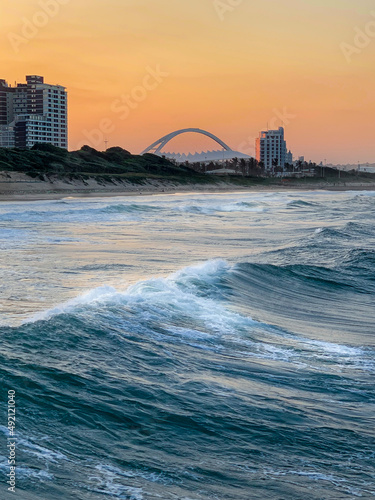 View from the blue waters of the Indian Ocean to the deep orange sunset sky with the famous Moses Mabhida Sadium arch in distant background. 