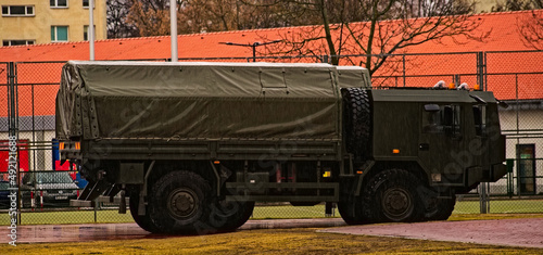 Wojskowe ciężarówki w kolorze khaki zaparkowane na placu ogrodzonym siatką stalową w czasie deszczu . Military trucks in Khaki color parked on a square fenced steel grid during rain. 