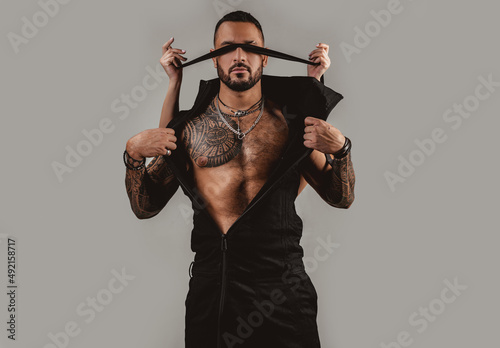 Brutal man with ribbon on eyes, serious handsome guy. Trust concept. Muscular macho man with athletic body. Female hands cover male eyes with rope.