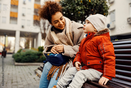 A cute little boy sitting outside with a young woman, nanny or caregiver, and telling something important.