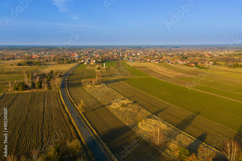 Droga na równinie pokrytej łąkami i polami uprawnymi. Jest słoneczny dzień. Widok z dużej wysokości, zdjęcie wykonano z użyciem drona.