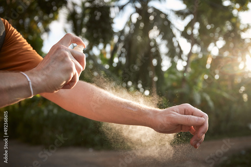 Prevention against mosquito bite in tropical destination. Man applying insect repellent on his hand against palm trees.