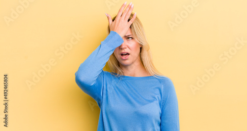 blonde caucasian woman raising palm to forehead thinking oops, after making a stupid mistake or remembering, feeling dumb