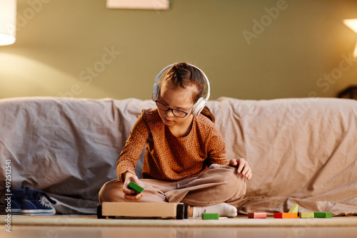 Portrait of young girl with down syndrome playing with toy blocks alone and wearing noise cancelling earphones, overstimulation concept, copy space