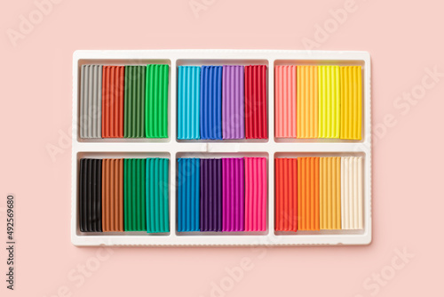 24 colors set of colorful plasticine sticks in white plastic packaging isolated on pink background. Pieces of multicolor plasticine modeling clay. Top view, closeup.