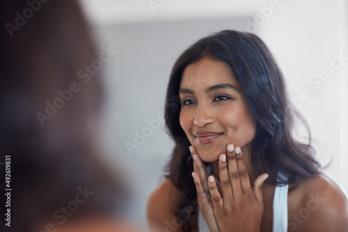 Your face will show you inner glow. Shot of a beautiful young woman admiring herself in the mirror at home.