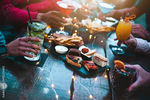 People hands holding cocktail glasses in bar table - Group of people eating appetizers enjoying happy hour time in pub restaurant - Beverage lifestyle concept