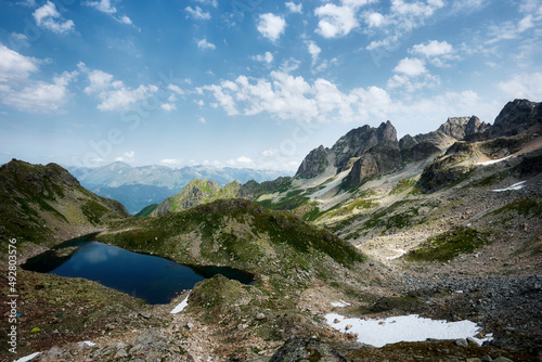 Panoramic view of turquoise Lake with surrounding sharp peaks mountains in the valley during sunny summer day. Arkhyz