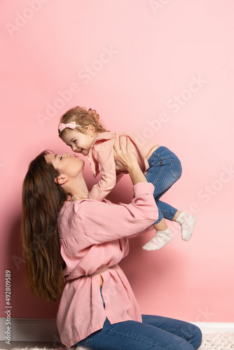 Portrait of young woman and little girl, mother and daughter isolated on pink studio background. Mother's Day celebration. Concept of family, childhood, motherhood