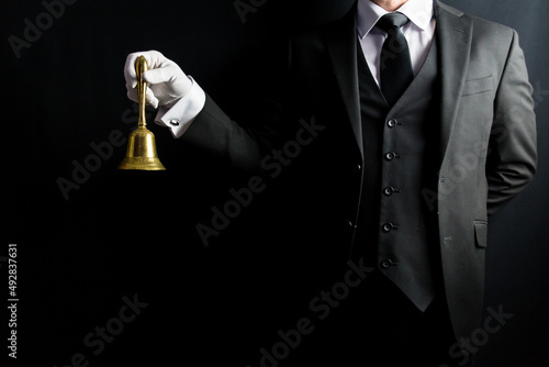 Portrait of Butler in Dark Formal Suit and White Gloves Holding Gold Bell. Professional Hospitality and Courtesy. At Your Service.