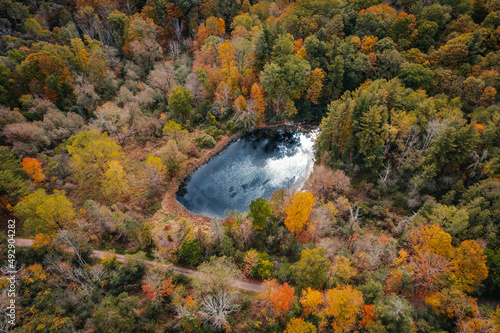 An aerial view of a secluded pond with blue water in an autumn forest with colourful leaves, in Hamilton, Ontario, Canada.