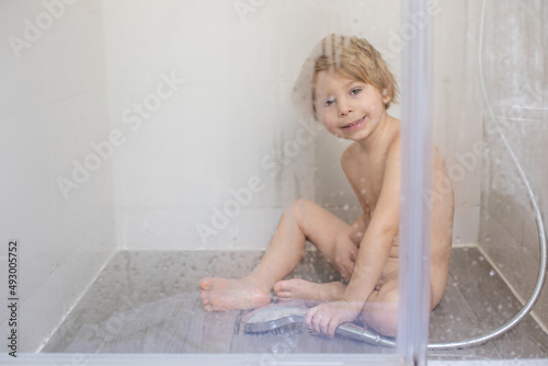 Blond child, sweet toddler boy in bathroom, taking shower, sitting on the floor, punished