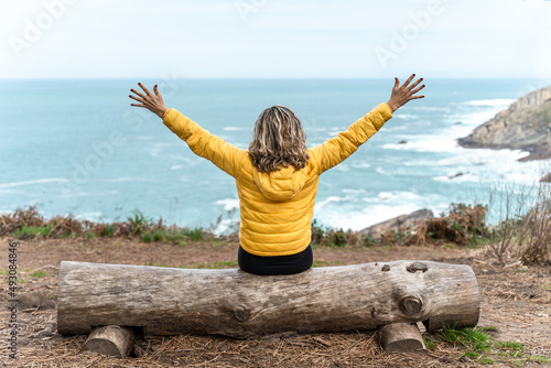 Woman open arms in front of the sea sitting on a log. Powerful woman tasting the freedom and happiness.