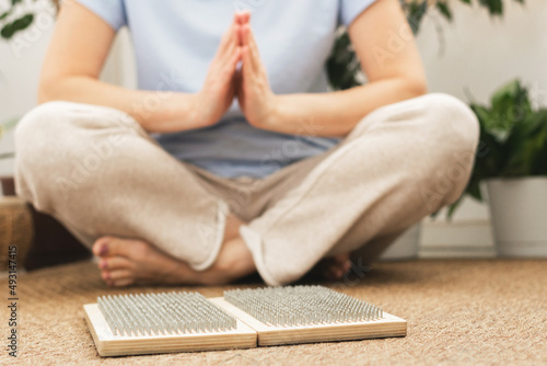 Woman of European appearance sits in lotus position with wooden sadhu board nails for sadhu practice.