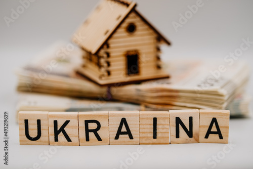 Napis Ukraina na tle domku stojącego na stosie banknotów